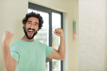 young crazy bearded man feeling happy, satisfied and powerful, flexing fit and muscular biceps,...