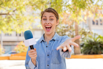 young pretty woman smiling happily and offering or showing a concept. presenter and microphone...