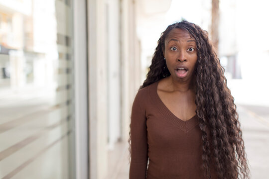 afro pretty black woman looking very shocked or surprised, staring with open mouth saying wow