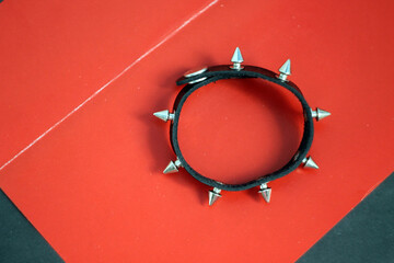 Black leather bracelet with metal spikes on a red background.