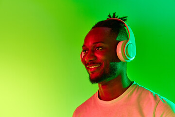 Image of young african man looking away in headphones and smiling over gradient colorful background...