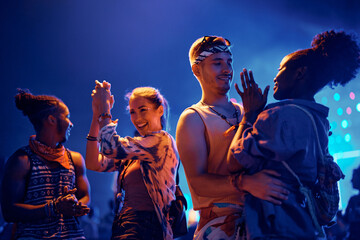 Group of happy friends having fun and dancing at summer music festival at night.