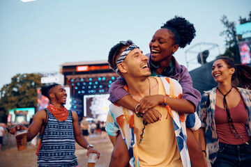 Happy man piggybacking his black girlfriend during open air music concert.