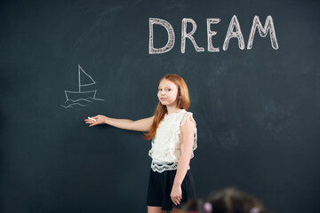 Little girl, child standing at chalkboard and drawing her dreamings. Imagination of children. Psychology and creative thinking. Concept of school, education, childhood, knowledge, lifestyle