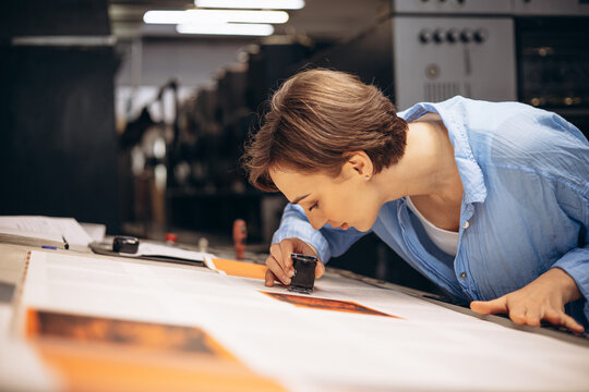 Woman typographer working in printing house with paper and magnifying lens
