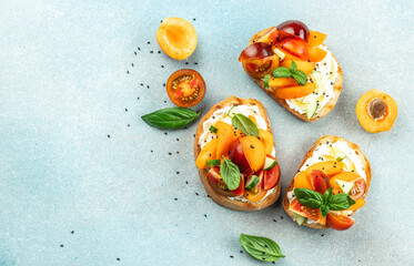 Open sandwiches with cream cheese, peaches, tomatoes and green basil leaves on a light background, Long banner format. top view - obrazy, fototapety, plakaty