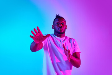 Frightened and withdraw african man looking at camera over colorful studio background in neon.