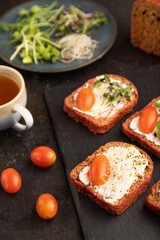 Red beet bread sandwiches with cream cheese, tomatoes and microgreen on black. side view, selective focus.