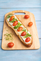 Long white bread sandwich with cream cheese, tomatoes and microgreen on blue. side view.