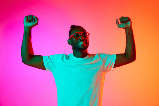 Strong and handsome african man in glasses looking away over pink-orange background in neon.