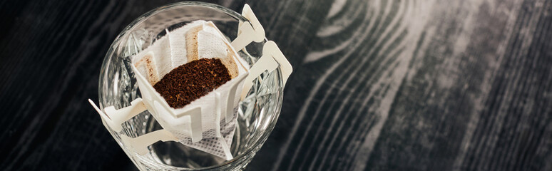 glass with aromatic ground coffee in filter bag on black table, pour-over brewing method, banner