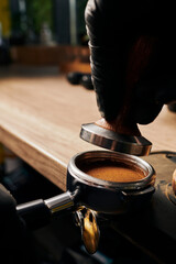 barista holding tamper above portafilter with grinded coffee, espresso, manual press, arabica