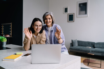 Cheerful mother and daughter showing hi gesture while having video call