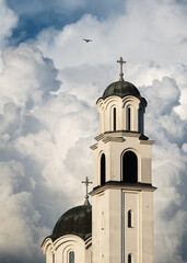 Orthodox church bell tower and pigeon flying next to it against big white cloud, symbol of God and faith