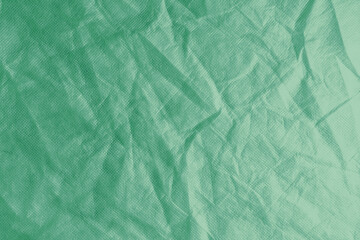 Wrinkled, crumpled green fabric texture background. Wrinkled and creased abstract backdrop of spunbond textile, wallpaper with copy space, top view.