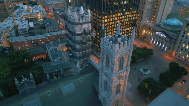 Deep pan up aerial bird eye view shot of Notre Dame basilica in Montreal looking down on the roof and towers in front of Place Jacque Cartier square surrounded by big buildings