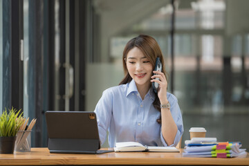 Happy beautiful smiling Asian businesswoman talking on a mobile phone while working in an office.