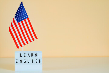USA flag and text Learn English online on a peach orange wall background. Mockup for presentation...