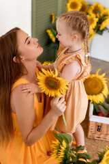 Tender mother and daughter happy together, hugging and having fun in the room full of sunflowers