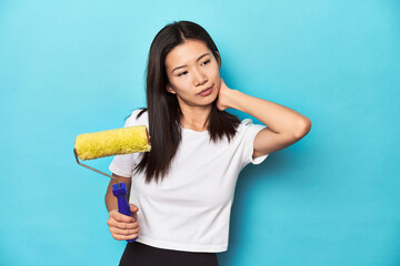 Young Asian woman with paint roller, DIY concept, touching back of head, thinking and making a choice.