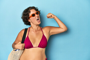 Young woman in bikini with beach bag raising fist after a victory, winner concept.