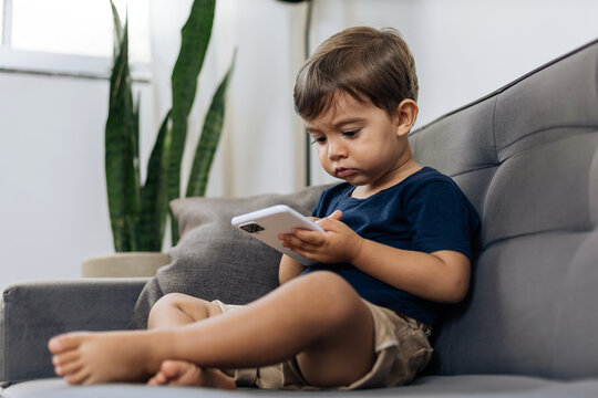 What age should a kid get a phone? Toddler boy using a smartphone on couch