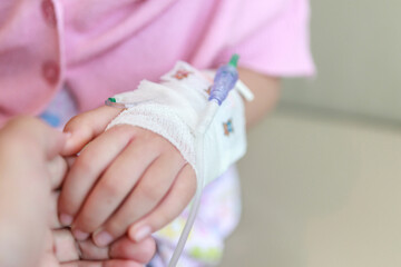 Mother holding child hand with saline IV solution in hospital