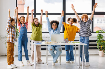 Fototapeta premium Teacher and cheerful schoolkids looking at laptop screen and celebrate successful completion of collective school work during online lesson