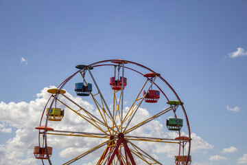 Detalhe de uma roda gigante colorida, com o céu azul ao fundo.