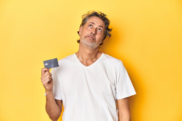 Man holding a credit card, yellow studio backdrop dreaming of achieving goals and purposes