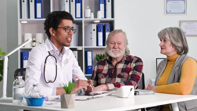 health care, an elderly man with his old wife at medical examination at black doctor measures blood pressure with tanometer in office
