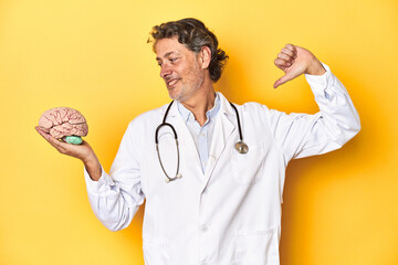 Doctor holding a brain model, yellow studio backdrop feels proud and self confident, example to...