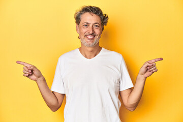 Middle-aged man posing on a yellow backdrop pointing to different copy spaces, choosing one of them, showing with finger.