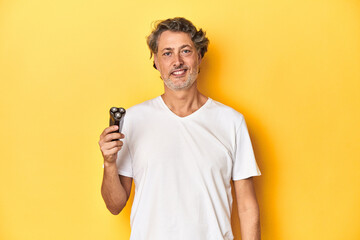 Man holding a razor, yellow studio background happy, smiling and cheerful.