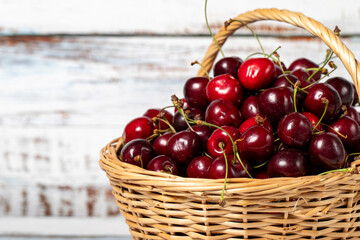 Fresh cherry in a wicker basket over wooden background. Cherry harvest season concept. Healthy and fresh fruit. Copy space. Empty space for text