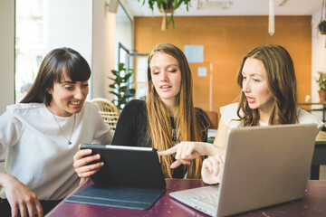 Three young beautiful caucasian millennials women indoor using technological devices like tablet and computer - business, technology, communication concept