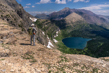 A hiker carrying a backpack watching a scene of a lake in a mountain cirque, Oldman Lake, Glacier...
