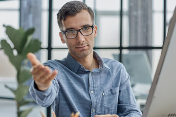 Young caucasian handsome man stretching hand at camera in greeting gesture.