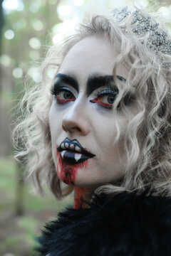 A woman in the form of a vampire or witch with white makeup on her face. woman looking at camera