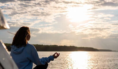 Rear view woman meditating on background of river and sunset.