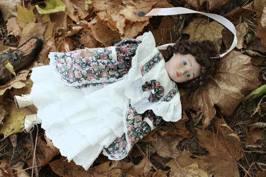 Doll toy lies on a ground between yellow autumn leaves in autumn park