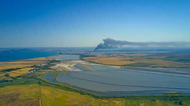 Panoramic drone shot of Burgas, Atanasov lakes and the Black Sea with a fire on the horizon, a large black plume of smoke
