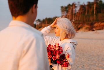 Love, romance, relationship, date. Young beautiful happy woman with a bouquet of flowers on beach at sunset, posing couple of lovers on sea