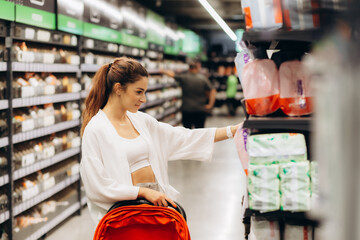 Pregnant woman buys diapers at the supermarket, portrait of young happy mother in shop