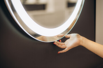 Woman's hand turns on the illumination of the bathroom mirror by touching the touch button on and...
