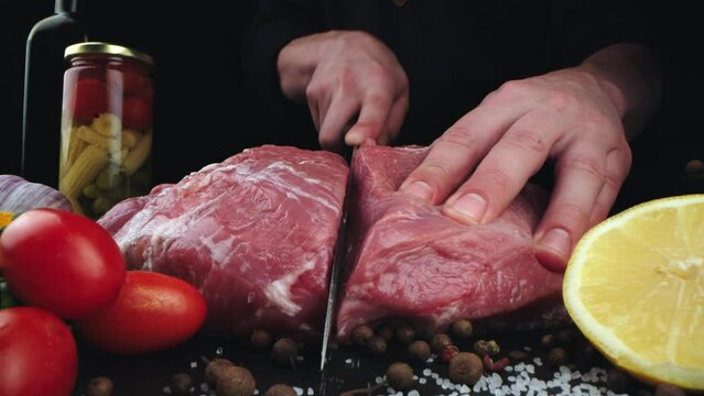 Chef cutting meat with a knife on kitchen table. Cooker is making a meal out of beef and vegetables on professional kitchen 4k footage