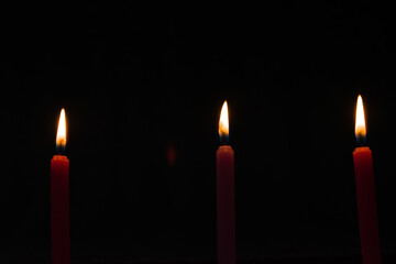 Three candles in a row lighten up in dark room. Photo taken from low angle