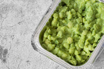 Mushy peas in a takeaway foil tray carton container. On a concrete background