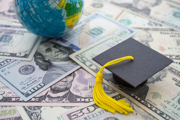 Graduation cap or hat on US dollars banknotes and globe world background. Abroad education, global...