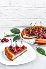Cheesecake with chocolate and cherry on a plate on a white table.